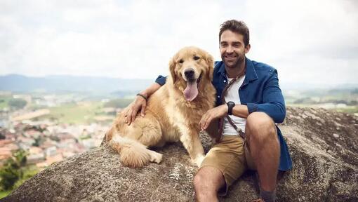 zdjęcie mężczyzny z psem rasy golden retriever siedzących na skale
